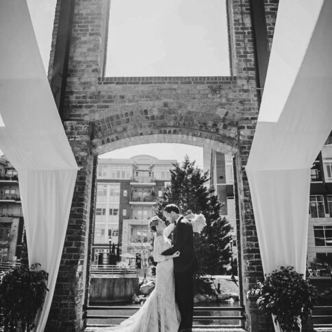 Standing on the ledge of an opening in the Wyche Pavillon in Greenville, SC, the happy bride and groom lovingly gaze at each other.