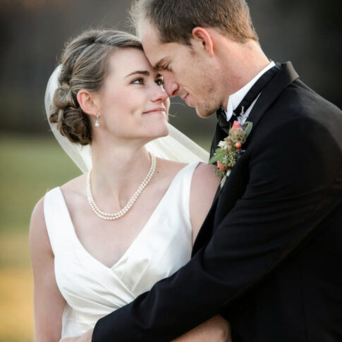 A new bride smiles up at her groom as they embrace.