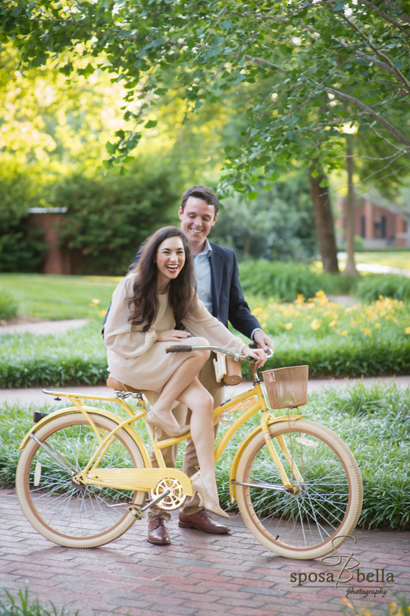 Bride-to-be laughs as her fiance steadies her bicycle. 