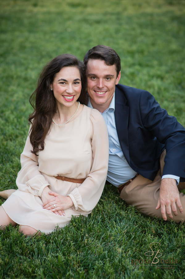 Engaged couple poses seated in the grass. 