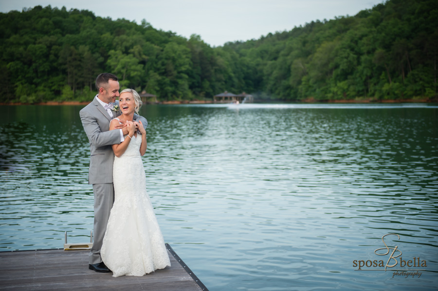 A happy couple hugs and laughs standing on a dock with Lake Keowee in the background.