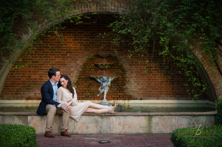 Soon-to-be husband gently kisses his fiance as the snuggle in front of a fountain. 