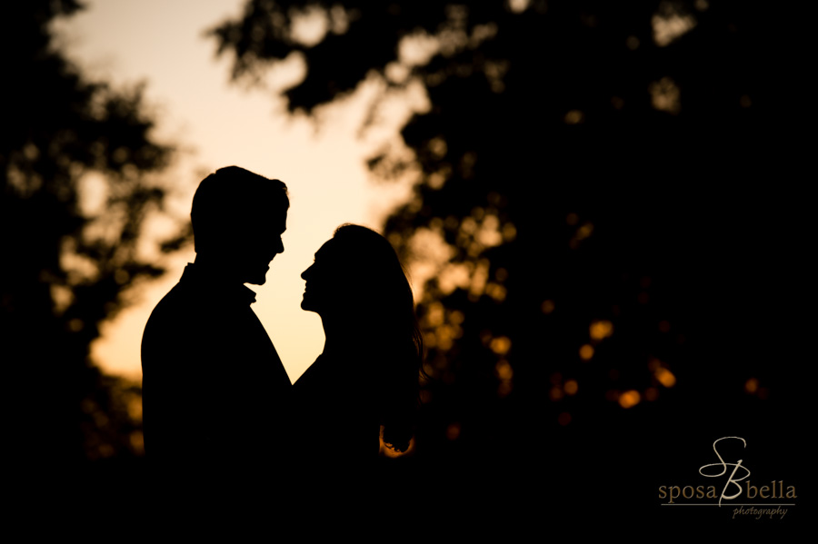 Engaged couple smiles and shares a gaze as their silhouette is framed by the sunset. 