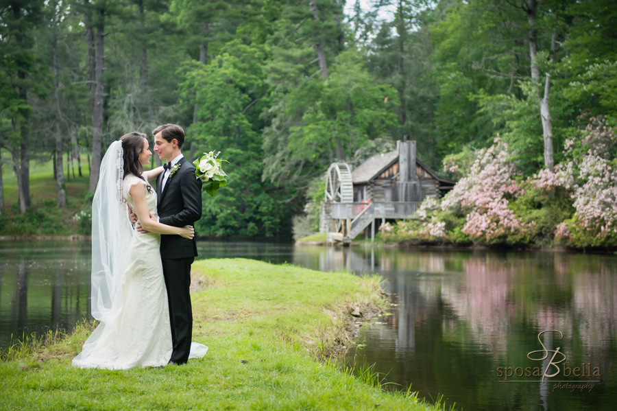 Bride and groom gaze sweetly at one another with a historic mill and pond in the background. 