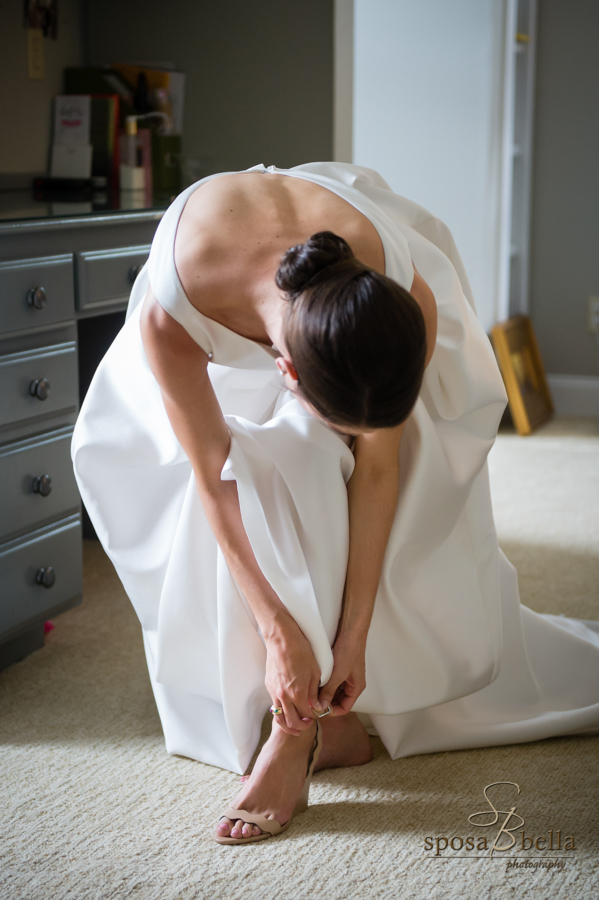 Bride leans over to fasten her shoe strap. 