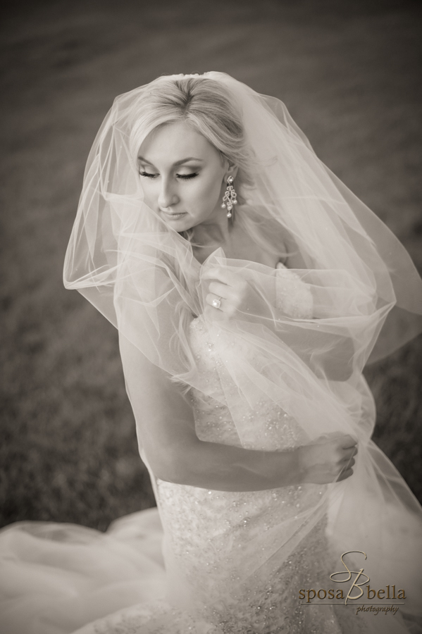 Moody black and white portrait of bride wrapping herself in her veil. 