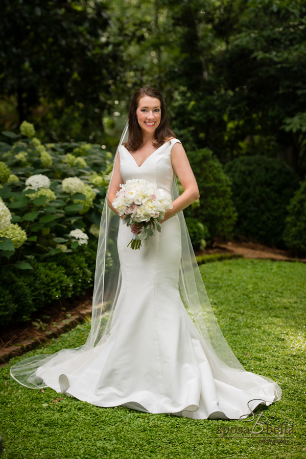 Bride smiles and poses among white hydrangeas matching her bouquet. 