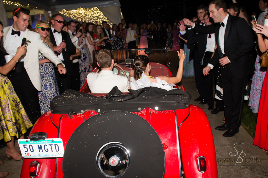 The bride and groom exit the reception in a bright red car. 