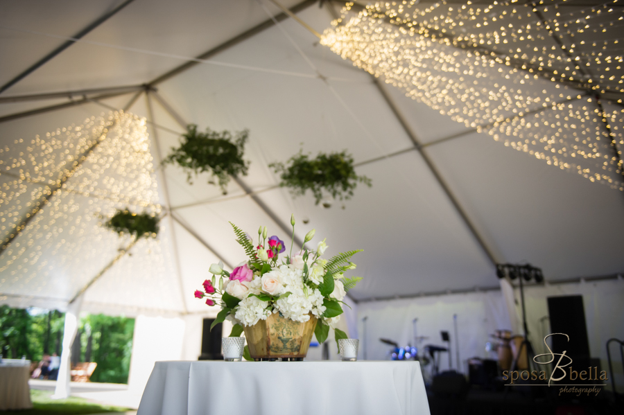 A shot of the flower arrangements at the reception with string lights hanging from the top of the tent in the background. 