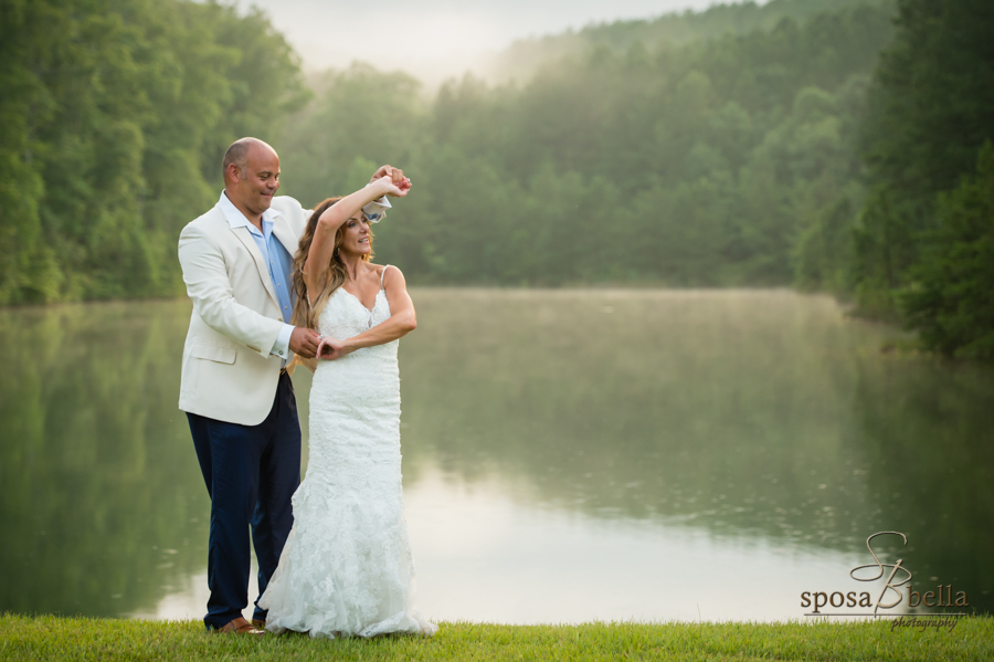 The groom spins his wife around as they dance by the water. 