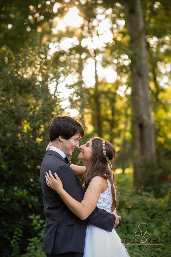 Bride and groom share a smile as the setting sun comes through the trees in the background. 