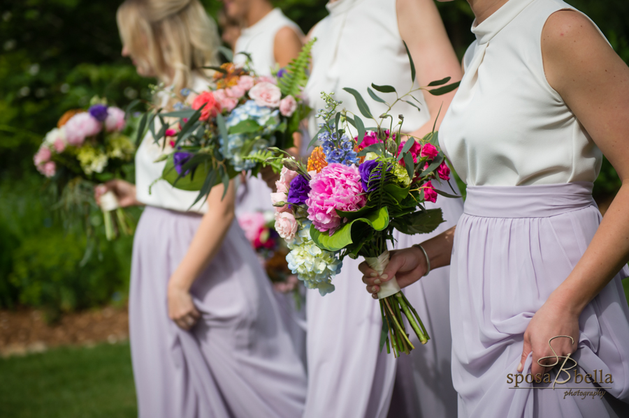 Bridesmaids walk in a line with bouquets in hand. 