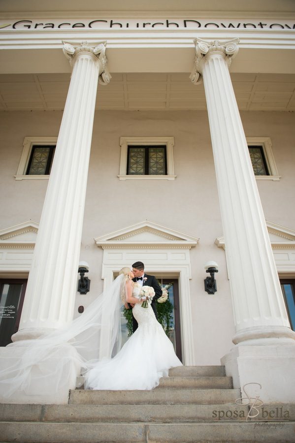 Couple kissing between the gigantic columns outside of Grace Church Downtown.