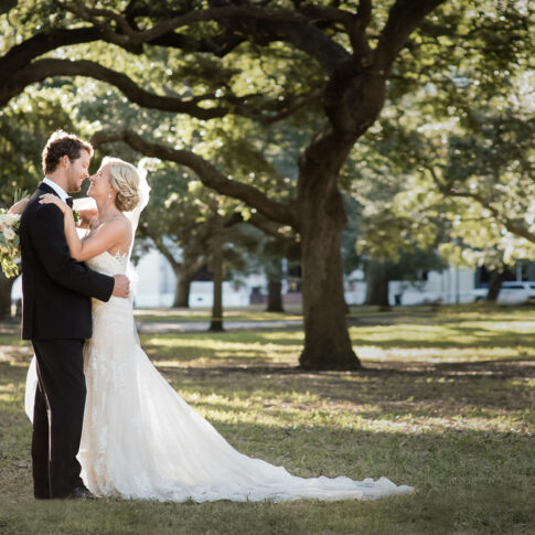 A bride hugs her groom under a canopy of back lit oak trees.